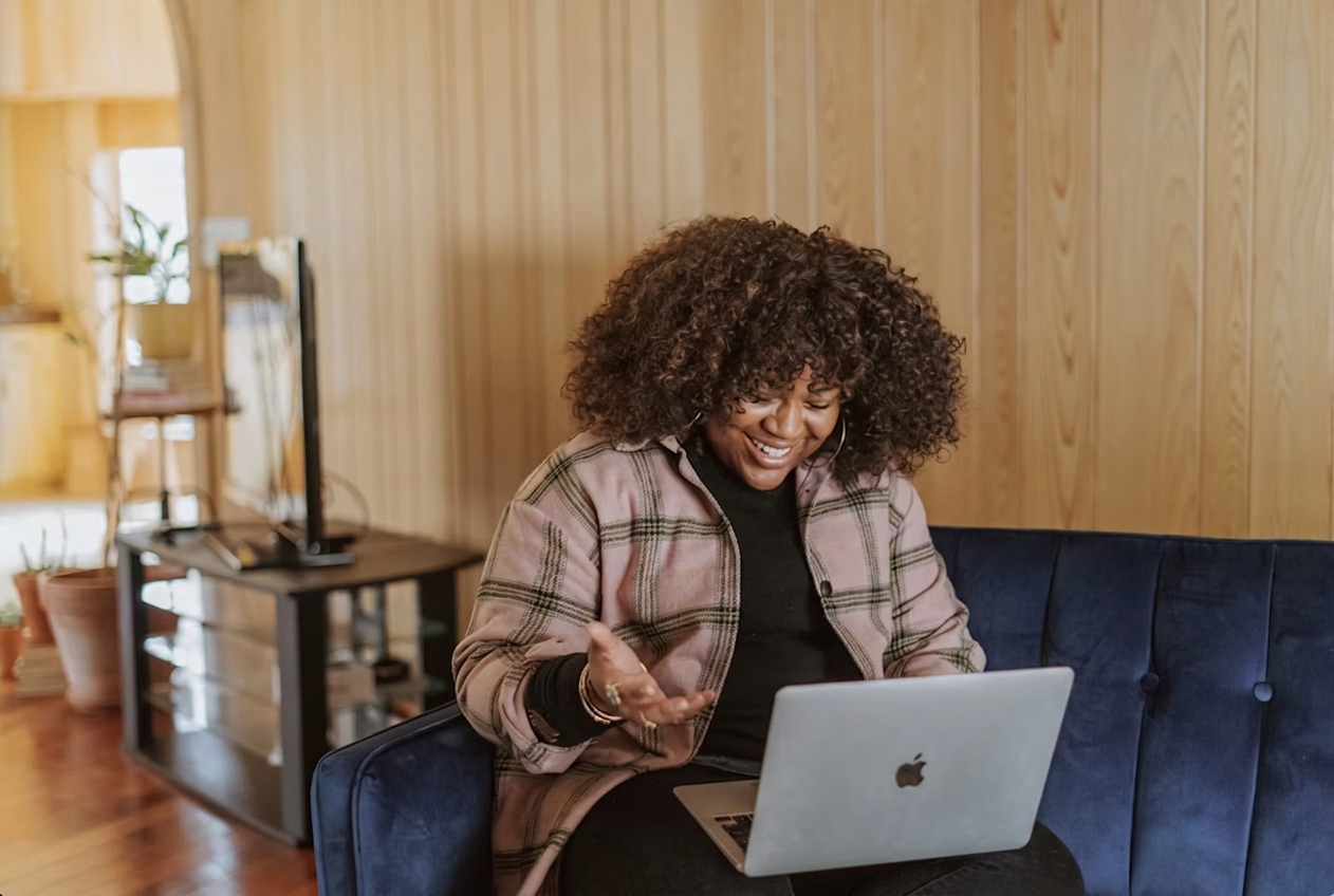 A smiling student learning on a MacBook while sitting on a blue velvet couch